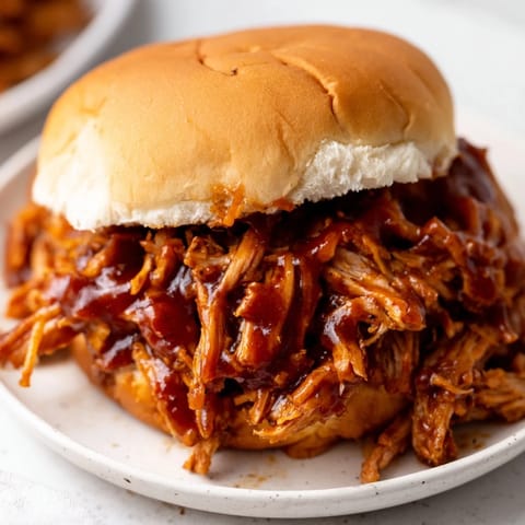 Slow-cooker Pulled Pork Sandwich with smoky barbecue sauce, glistening meat, and soft buns ready for a casual backyard dinner.