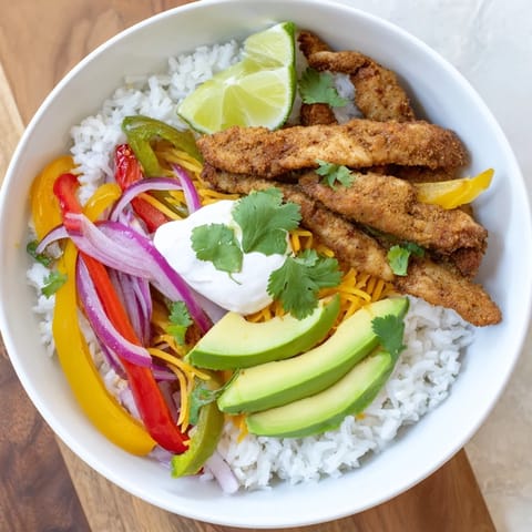 Fork-tender seasoned chicken strips and sautéed peppers and onions piled high on fluffy rice in a vibrant Chicken Fajita Bowl, finished with fresh garnishes.