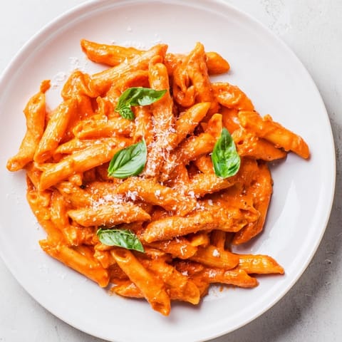Creamy roasted red pepper pasta garnished with fresh basil and grated Parmesan on a rustic wooden table.  