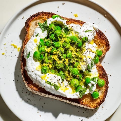 A vibrant pea and mint ricotta toast garnished with lemon wedges and olive oil, ready for brunch.