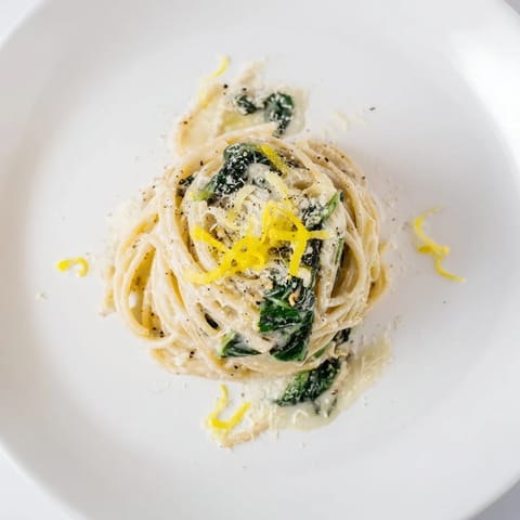Fork-ready Creamy Lemon Spinach Spaghetti tossed with wilted spinach and garlic, plated alongside a glass of chilled white wine.