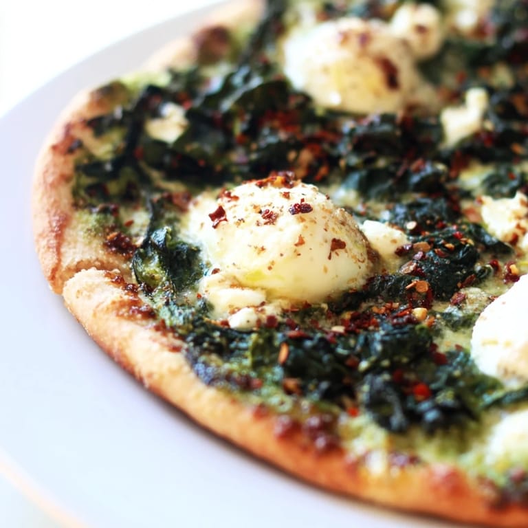 A close-up of a slice of spinach ricotta pizza, showcasing creamy ricotta and melted mozzarella over garlic butter.  