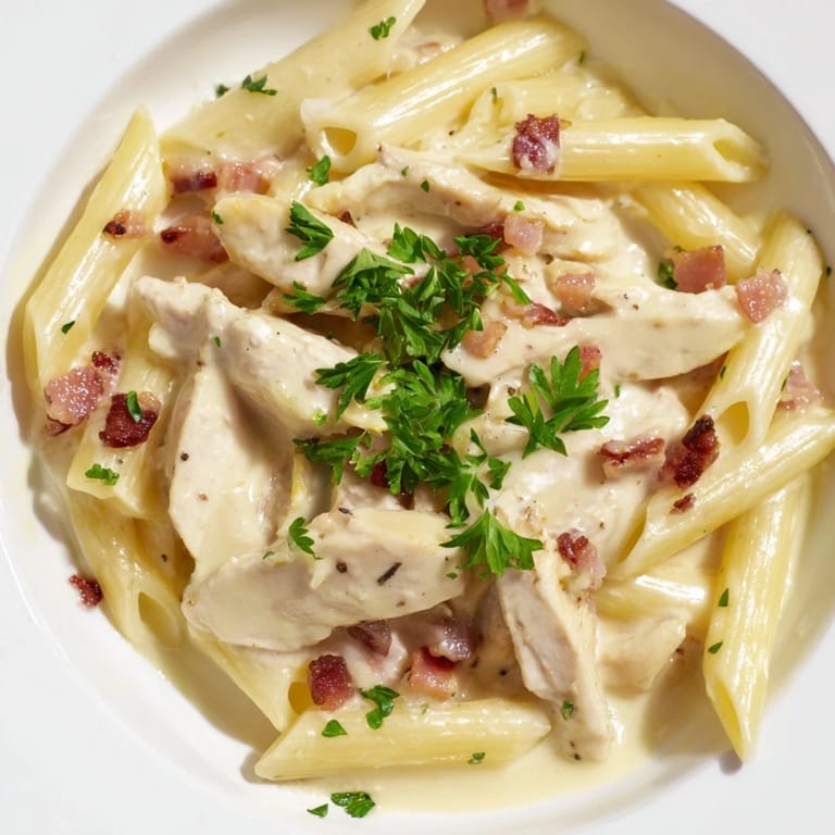 A close-up of Creamy Chicken Bacon Penne with fresh parsley garnish, showcasing golden-brown chicken pieces and smoky bacon in a luscious cream sauce.