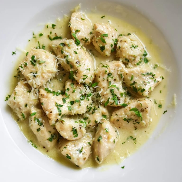 A close-up of Creamy Garlic Chicken Bites drizzled with rich sauce and a sprinkle of red pepper flakes.