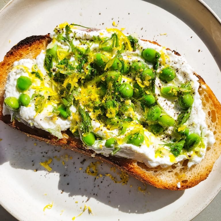 Pea and mint ricotta spread on crunchy sourdough, topped with lemon zest for a refreshing breakfast or lunch.