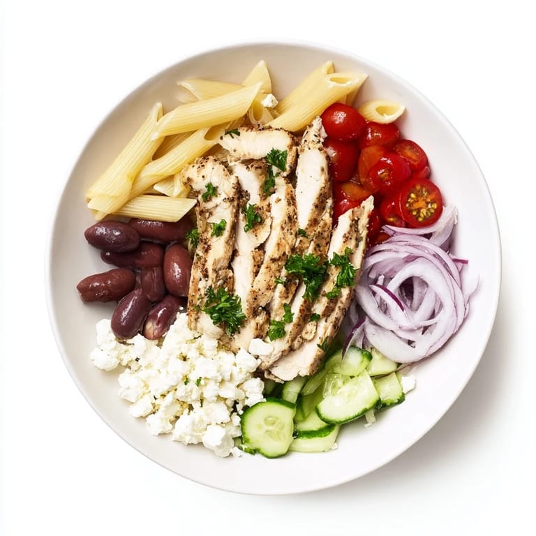 Colorful Greek Chicken Pasta Bowl garnished with parsley, red onion, and Kalamata olives on a rustic wooden table.